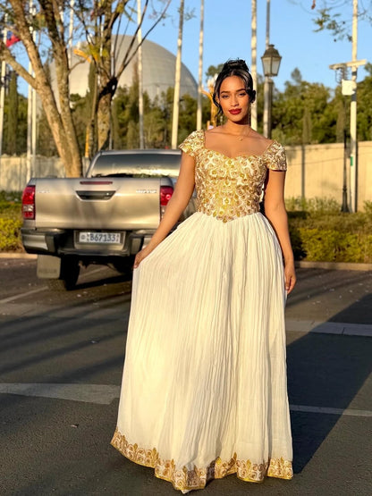 Woman in a gold and white Ethiopian cultural dress standing on a street with a car and trees in the background.