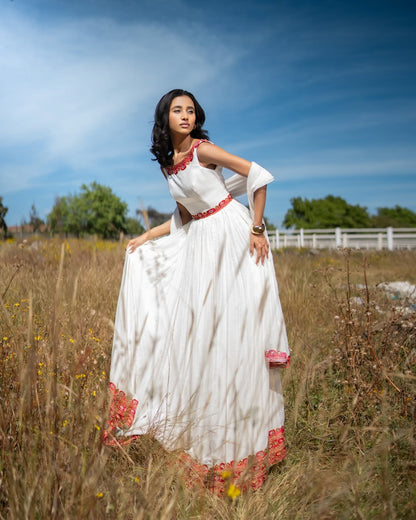 Woman in a habesha kemis with red accents standing in a field with a blue sky.