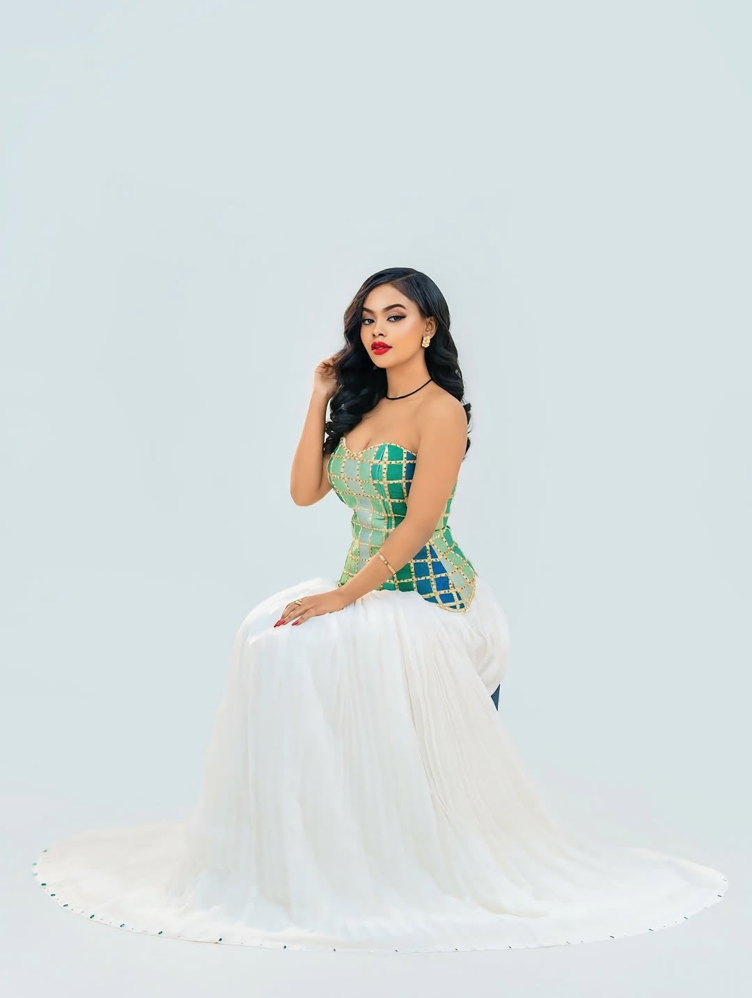 Woman in a green and white Ethiopian cultural dress posing against a light gray background