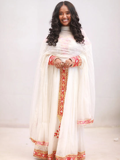 Woman wearing a white traditional Ethiopian Dress with red and gold patterns on a plain background