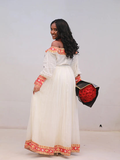 Woman wearing a traditional Ethiopian Dress with white top and red and orange patterns, holding a black clutch with red floral design.