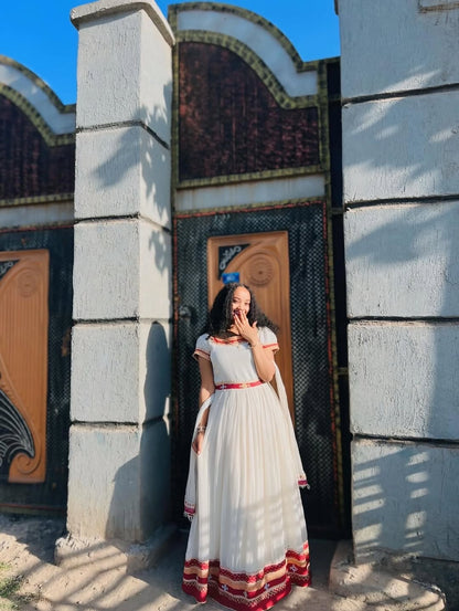 Woman in a Ethiopian dress with red accents standing in front of a decorative building entrance.