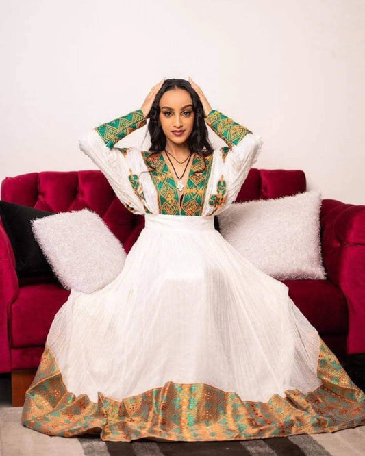 Woman in a traditional habesha outfit sitting on a red couch with white and black cushions.