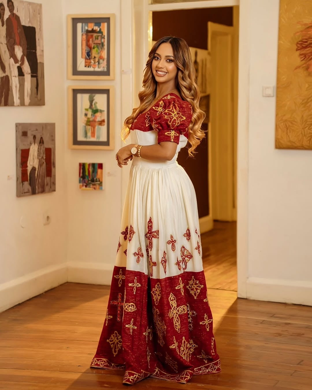 Woman in a red and white embroidered Ethiopian cultural dress standing in an art gallery.