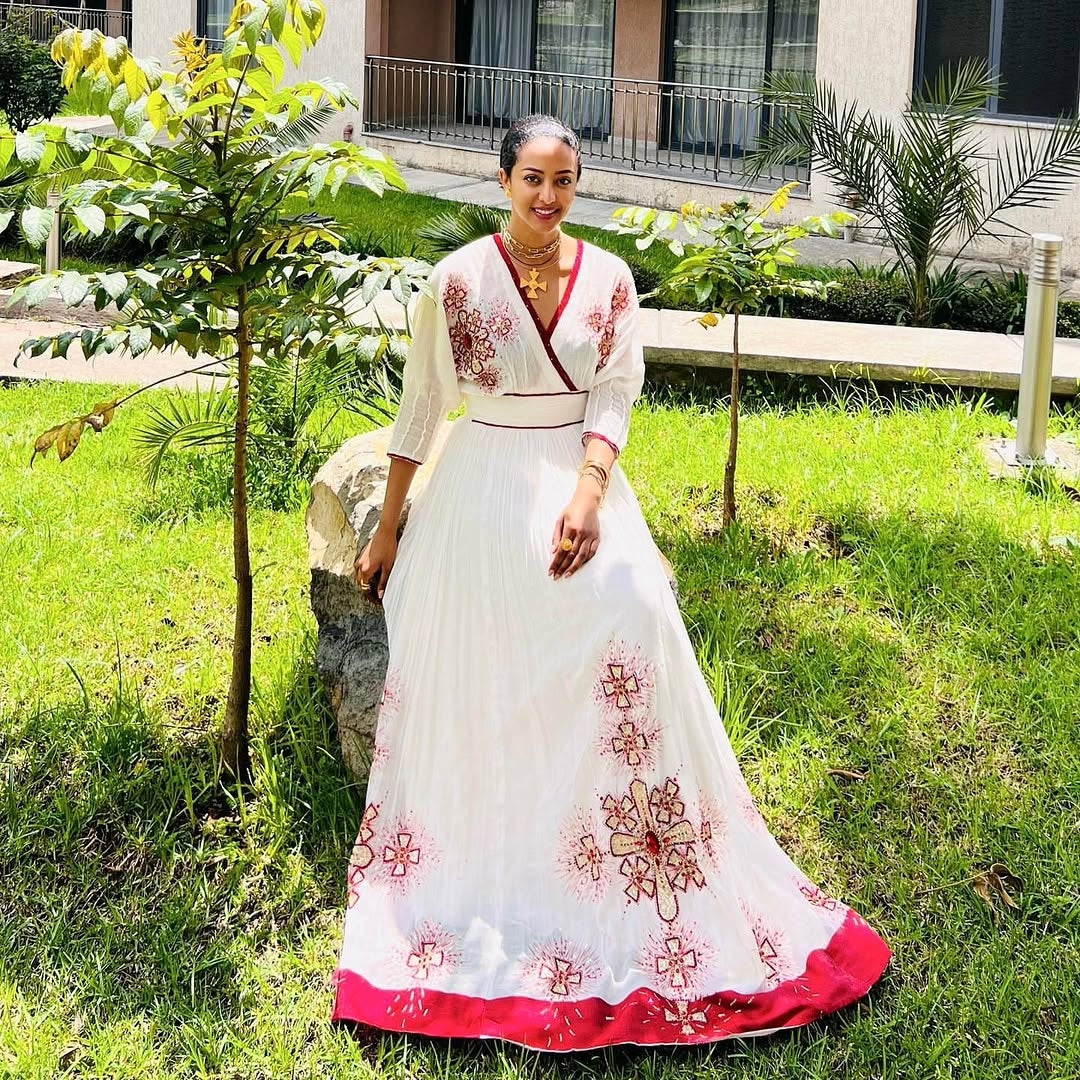 Woman in a white and red  Habesha Zuria  embroidered dress standing outdoors on grass.