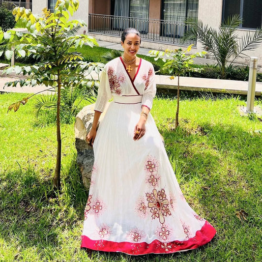 Woman in a white and red  Habesha Zuria  embroidered dress standing outdoors on grass.
