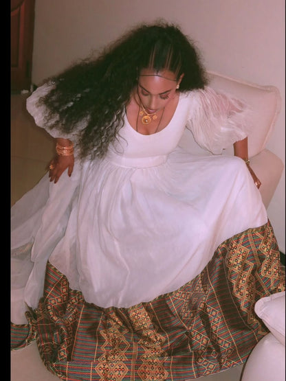 Person wearing a white dress with a patterned bottom half sitting on a couch.