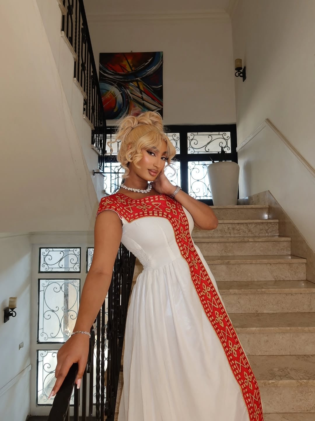 Woman in a white and red dress standing in a staircase interior.