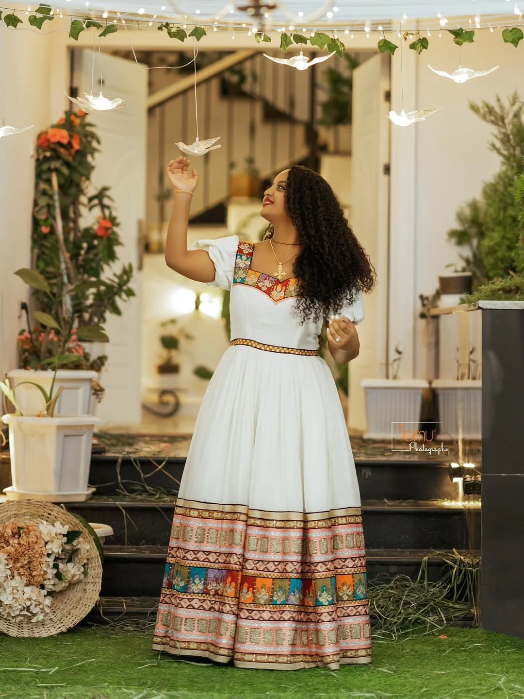 Woman in a Brown Habesha Zuria standing outdoors with plants and lights in the background