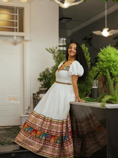 Woman in a Brown Habesha Zuria with colorful patterns standing in an indoor setting with plants.