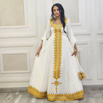 Woman wearing a white dress with gold embroidery in an elegant room.