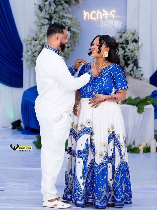Couple in traditional Ethiopian wedding dress at a decorated event with floral arrangements.