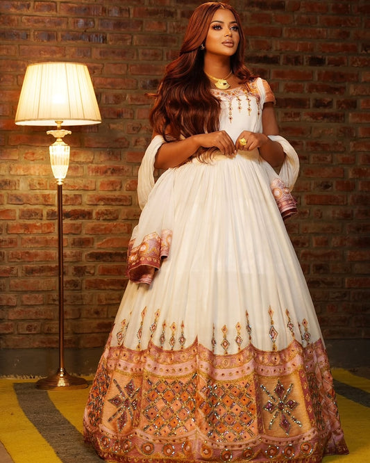 Woman in a white and orange traditional Ethiopian Traditional Dress standing against a brick wall.