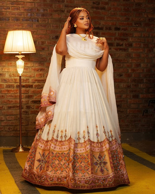 Woman in a white and patterned Ethiopian Traditional Dress standing against a brick wall.