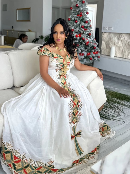 Woman in a white Ethiopian Libs with colorful patterns sitting in a modern living room.