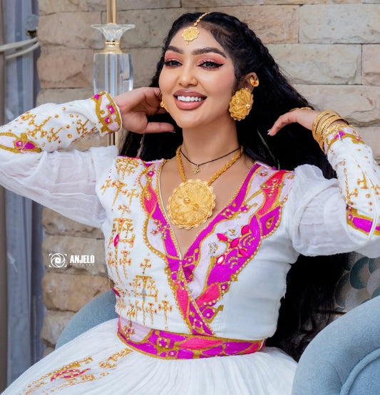 Woman in Ethiopian Zuria  with gold and pink details, sitting outdoors.