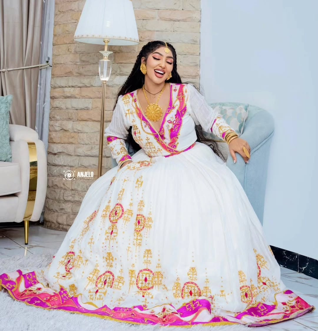 Woman in a white and pink Ethiopian Zuria  sitting on a couch in a living room.