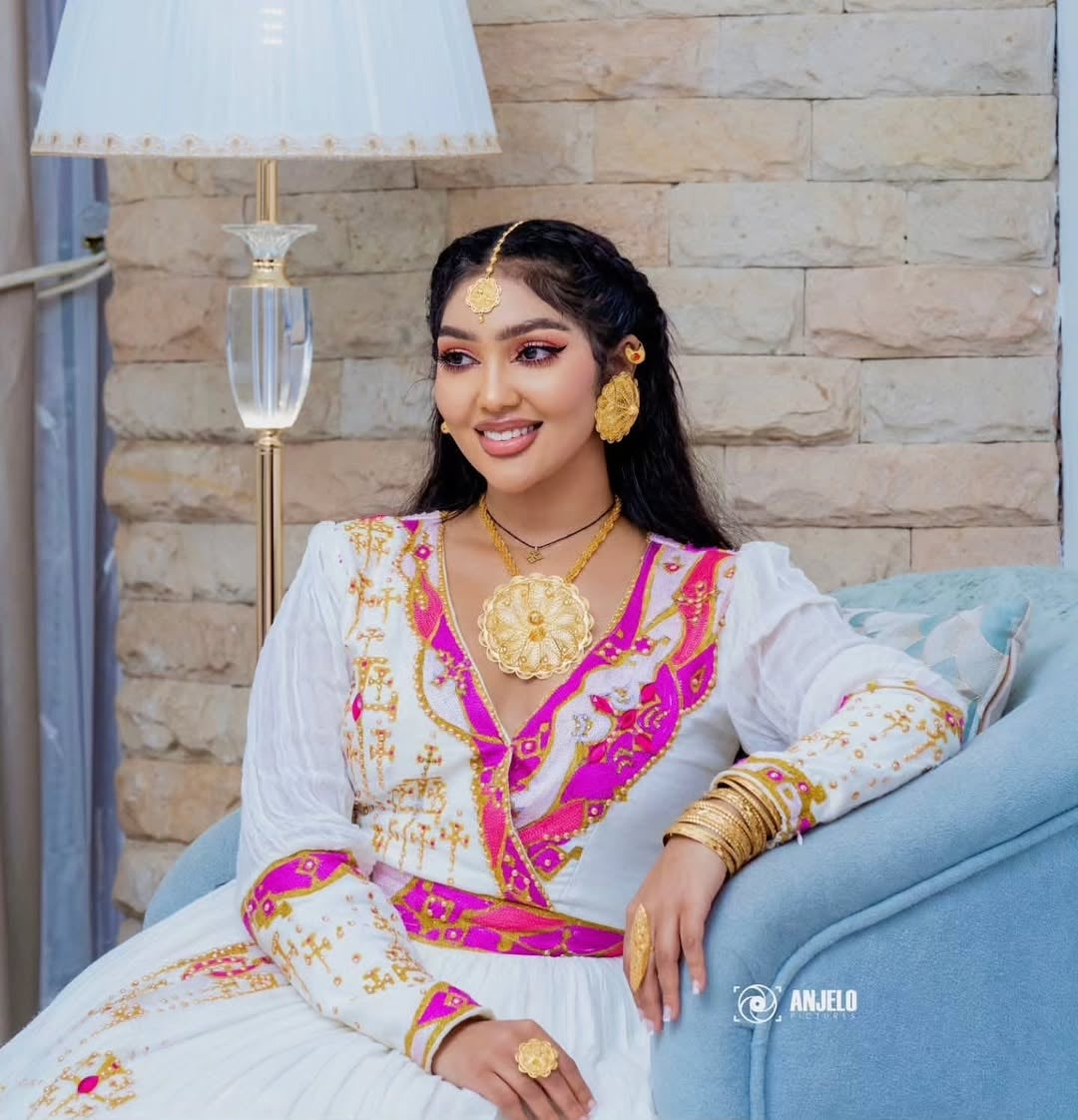 Woman in Ethiopian Zuria with gold jewelry sitting on a couch.
