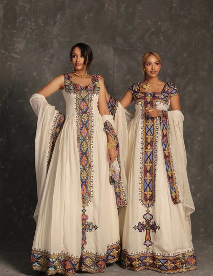 Two women modeling traditional South Asian salwar kameez Ethiopian Dress  with intricate multicolor geometric embroidery on an off-white base, set against a dark textured studio backdrop.