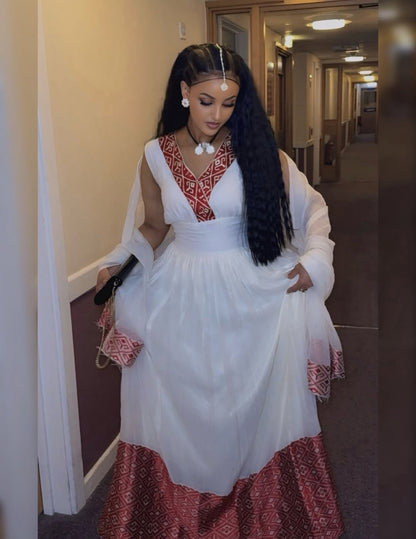 Woman in a white and red traditional habesha kemis standing in a hallway.