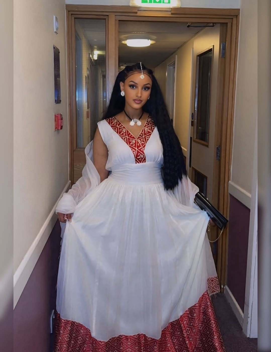 Woman in a white and red habesha kemis standing in a hallway