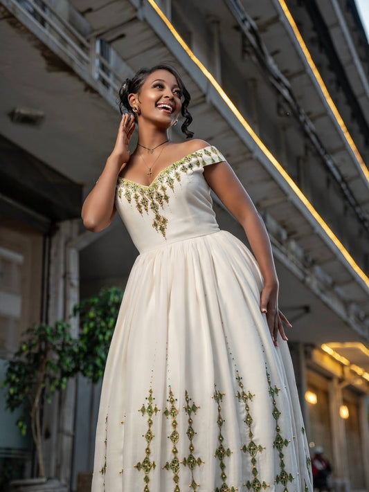 Woman in a white gown with gold embroidery standing indoors.