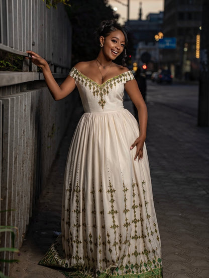 Woman in a white and gold habesha dress in an elegant interior setting.