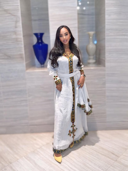 Woman in a white and gold traditional outfit standing in a room with decorative vases.
