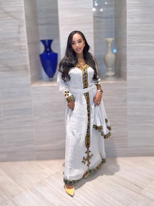 Woman in a white and gold traditional outfit standing in a room with decorative vases.