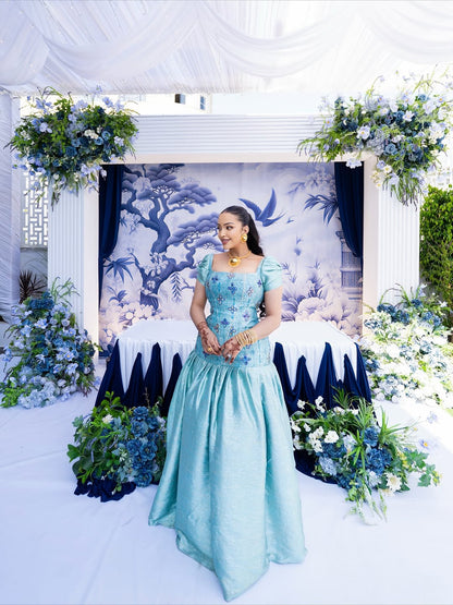 Woman in a light blue habesha kemis  standing in front of floral decorations and a decorated archway.