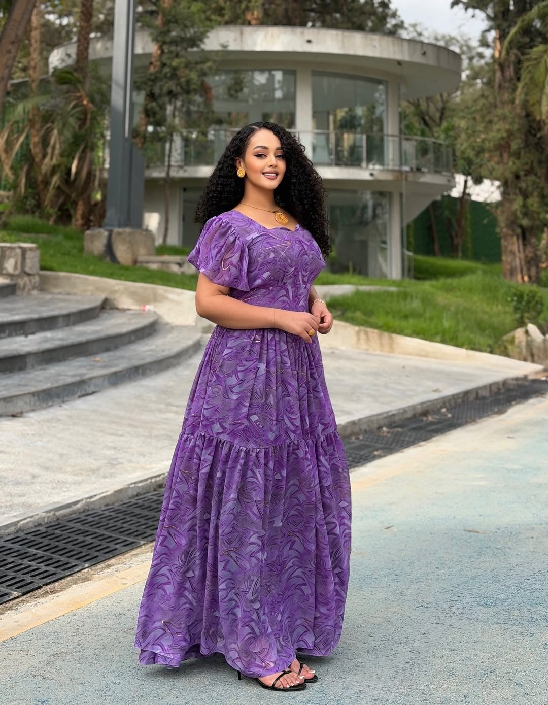 Woman in a purple dress standing outdoors with modern architecture in the background