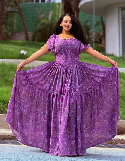 Woman in a purple dress with a floral pattern standing outdoors.