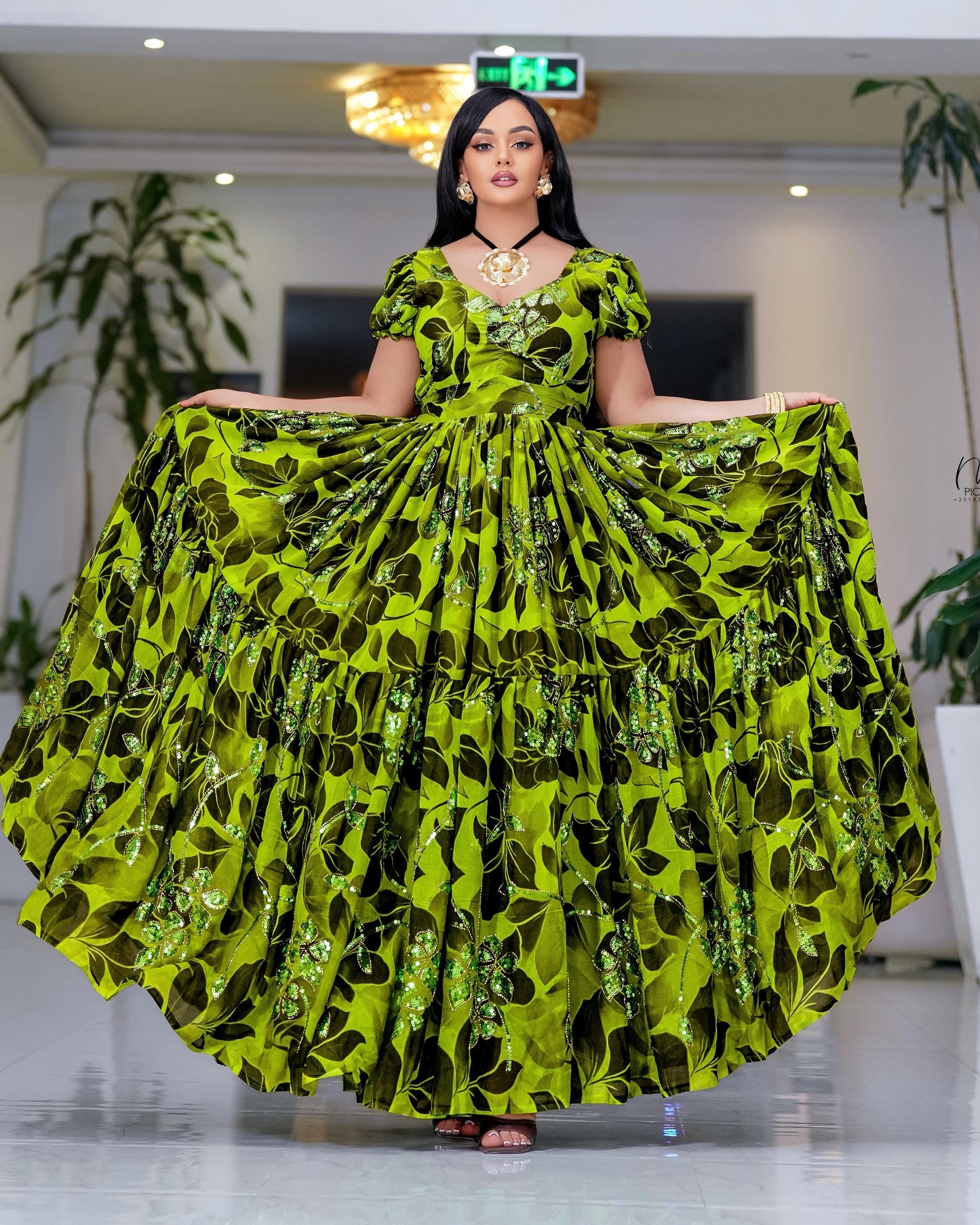 A woman modeling a voluminous habesha chiffon with a bright lime green and black leaf pattern, holding the skirt outwards in a showroom.