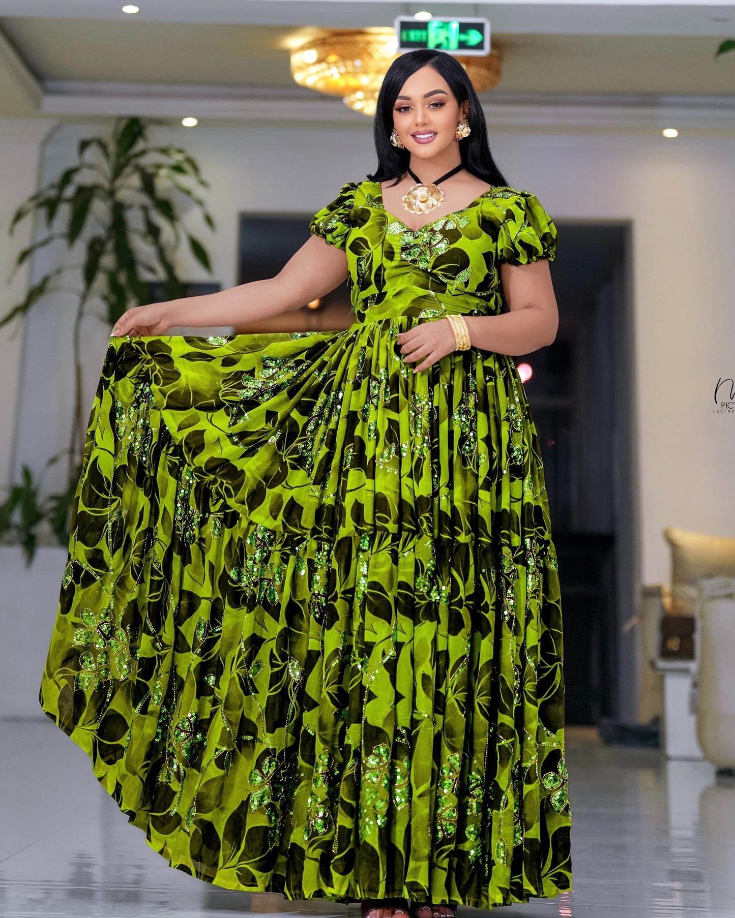 A woman modeling a vibrant lime green and black patterned habesha chiffon with sequined details, standing in an indoor showroom.