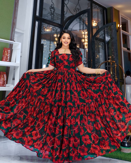 A woman modeling a red and black floral tiered Habesha Chiffon , holding out the sides of the skirt to show its full volume. The dress features a square neckline, short puff sleeves, and a dramatic, flowing silhouette with a red and black floral pattern.