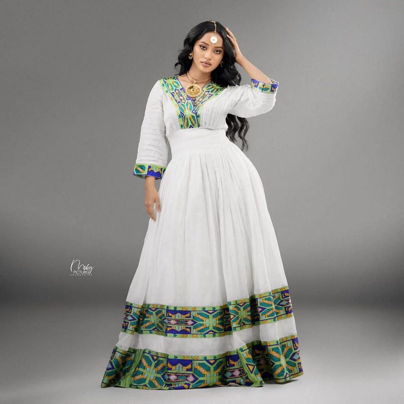 Woman wearing a green ethiopian cultural dress with colorful patterns on a gray background