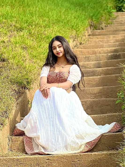 Woman in a traditional habesha dress sitting on stone steps with greenery in the background