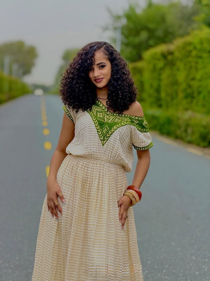 Woman in a patterned habesha dress standing on a road with greenery in the background