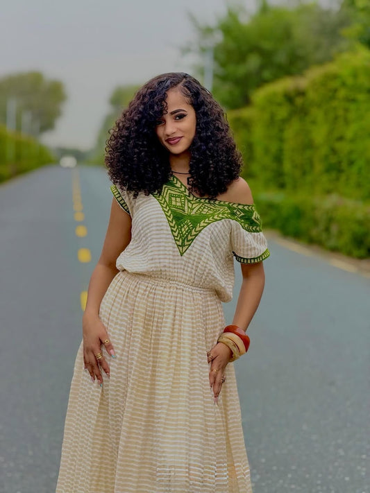 Woman in a patterned habesha dress standing on a road with greenery in the background