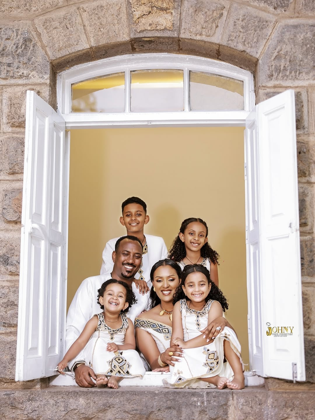 Family of six posing Family Habesha Set in front of an open window with a stone wall background