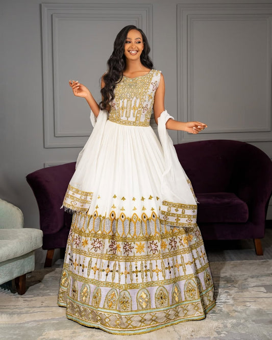 Woman wearing a white and gold Ethiopian wedding dress in an elegant room with purple chairs.