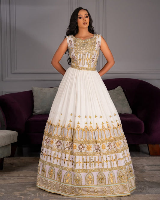 Woman wearing a white and gold Ethiopian wedding dress in a room with a purple couch.