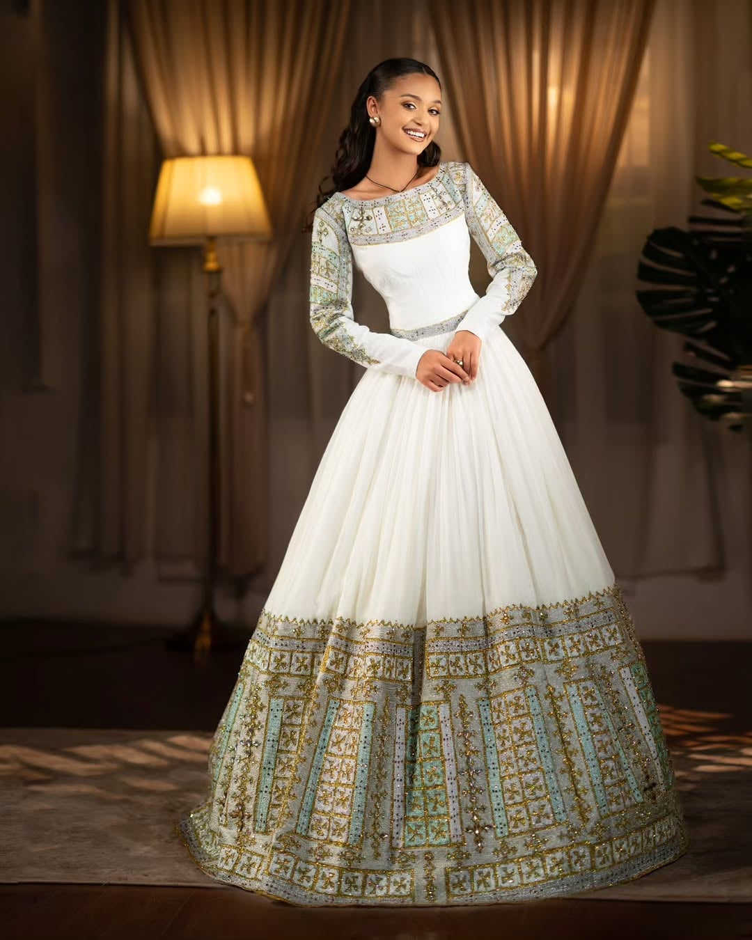 Woman wearing a white and Green Habesha Libs with intricate patterns in a warm-toned room.