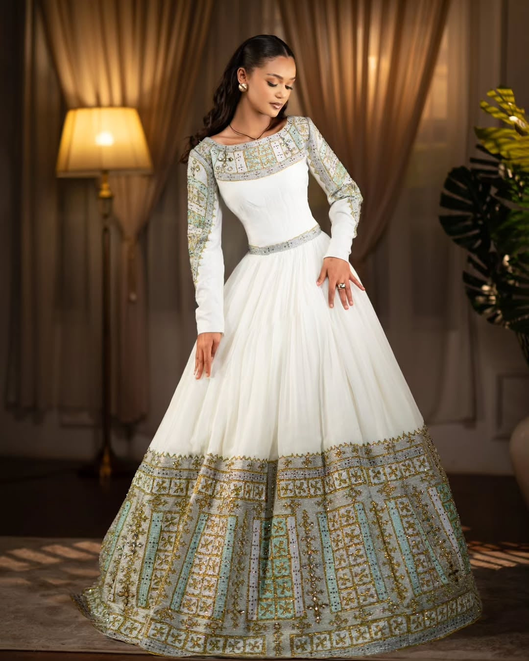 Woman wearing a white and gold Green Habesha Libs in a warm-toned room.