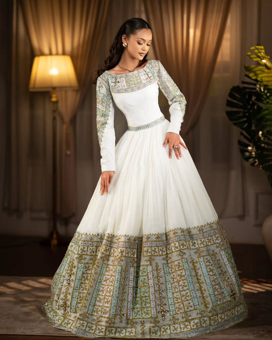 Woman wearing a white and gold Green Habesha Libs in a warm-toned room.