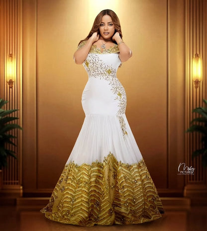 Woman wearing a white and gold evening gown against a warm-toned wall.