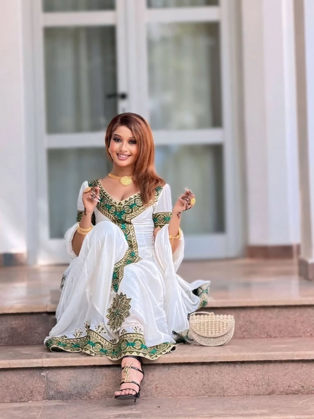 Woman in a white and green traditional outfit sitting on steps.