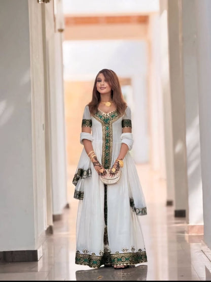 Woman in a white and green traditional outfit standing in a modern indoor setting.