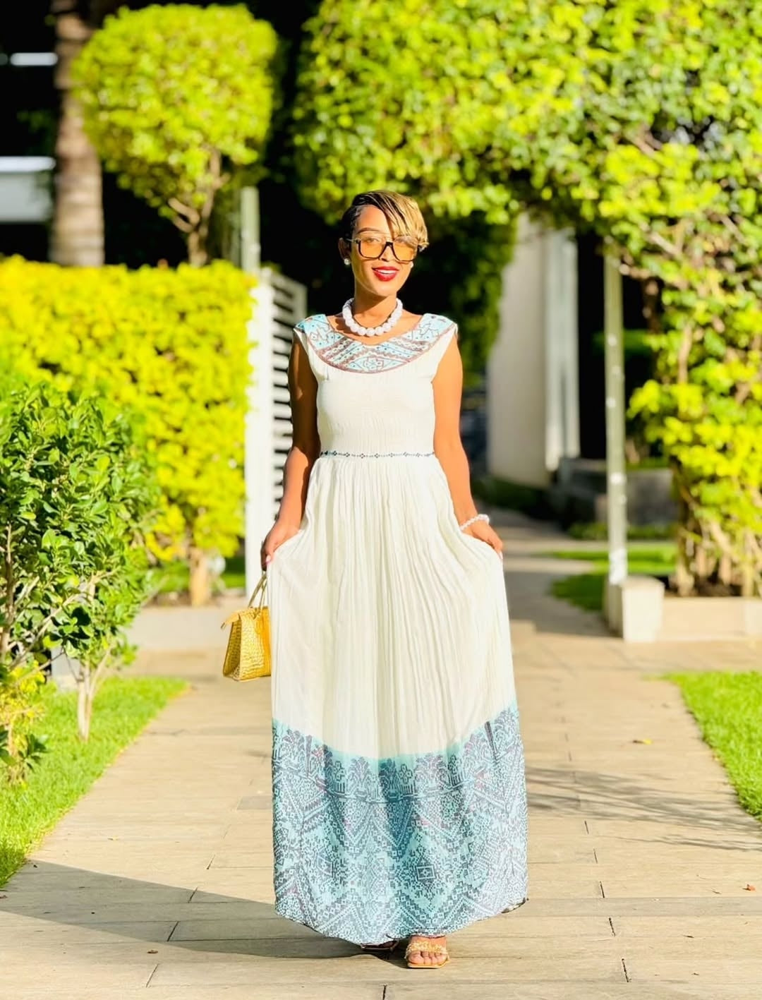 Woman in a white and blue dress walking on a sidewalk with greenery in the background