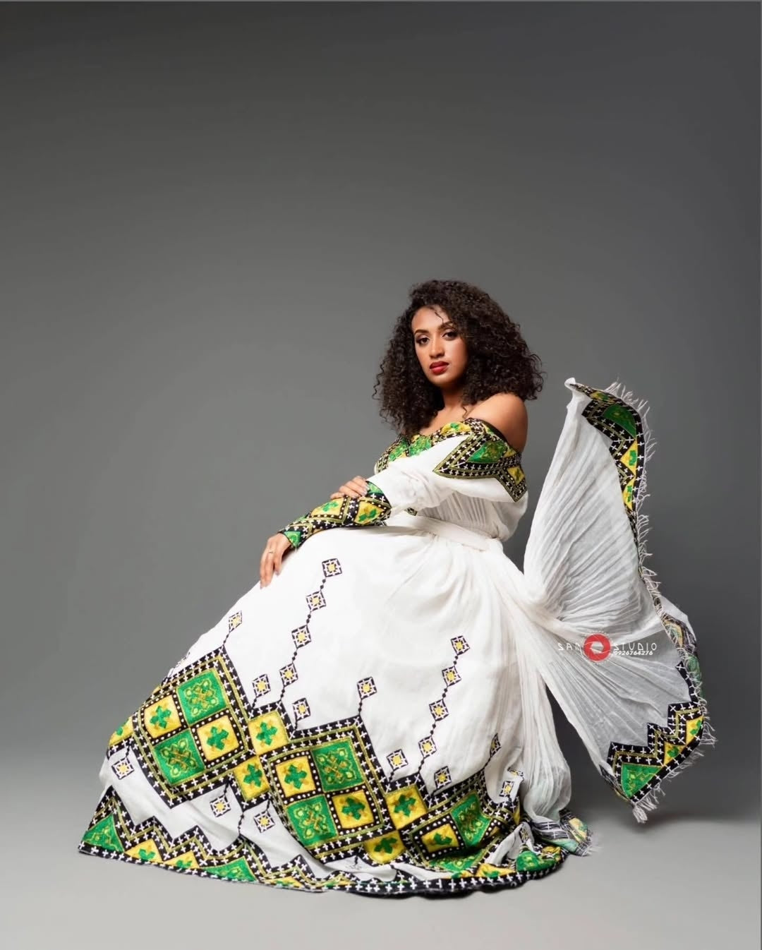 Woman wearing a white Habesha Zuria with green and yellow patterns on a gray background